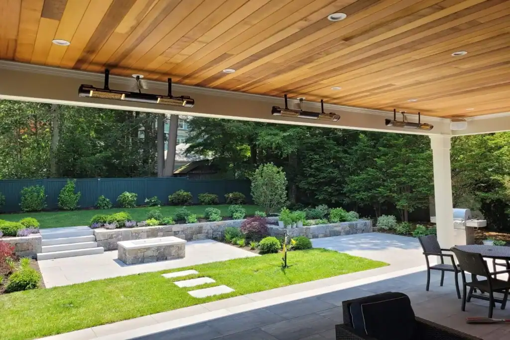 View of ceiling-mounted outdoor Solaira heaters underneath a residential covered porch with a view of a well-manicured backyard in Brookline, MA