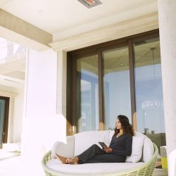 Woman seated outside on her balcony with an Infratech WD flush-mount heater installed above her